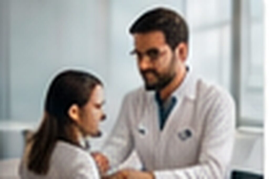 Médico gravando conteúdo educativo com smartphone e microfone em consultório real, postura natural, equipe pequena ao fundo